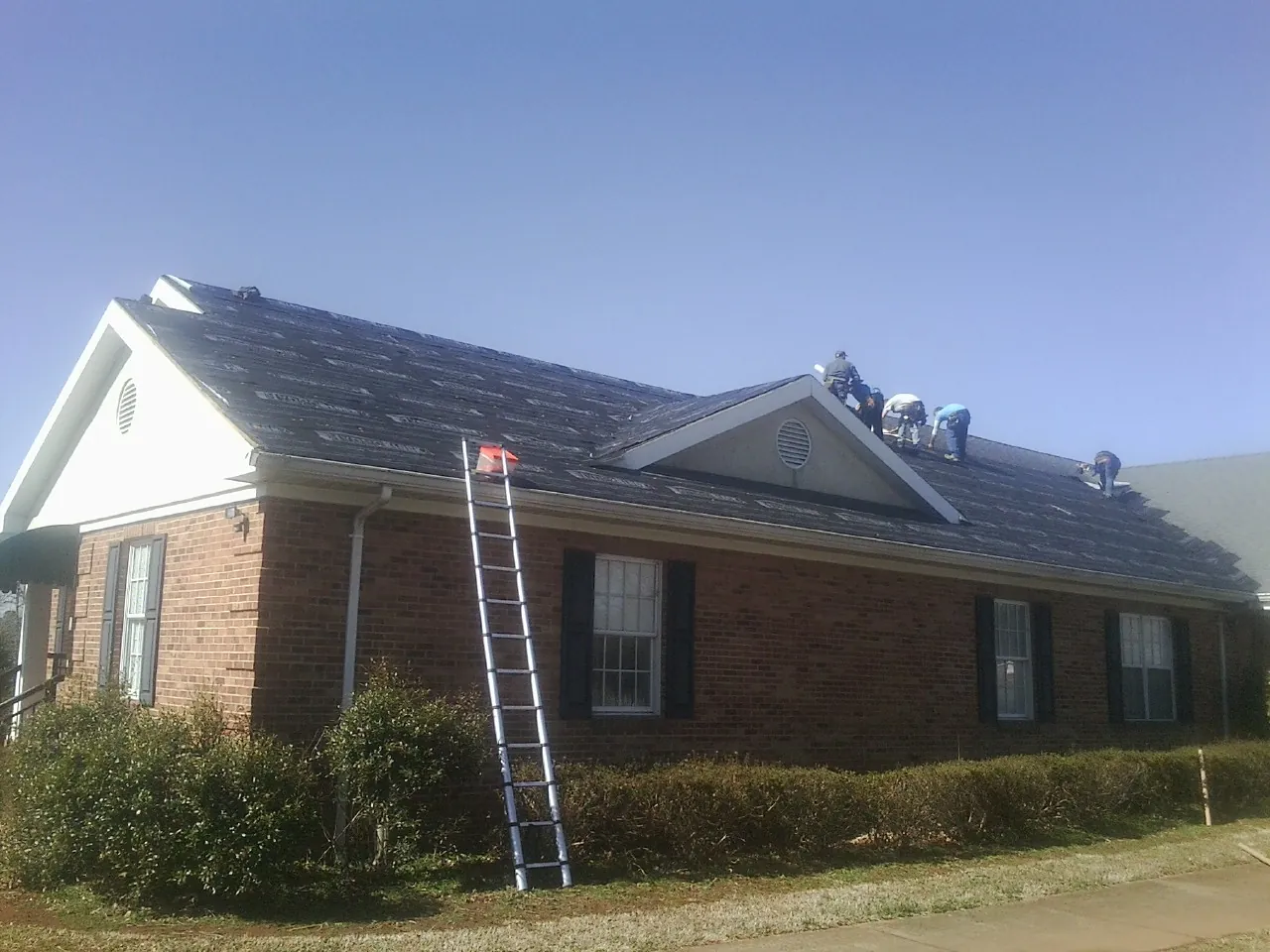 Crew tearing shingles off a brick ranch roof with a ladder set — Metal Roof Repair work by our crew in Santa Fe
