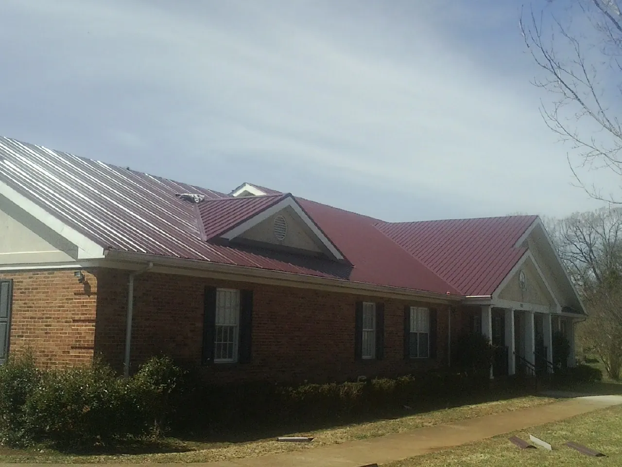 Red metal roof with gabled entries on a long brick building, from a Hail Damage Roof Repair job in Santa Fe