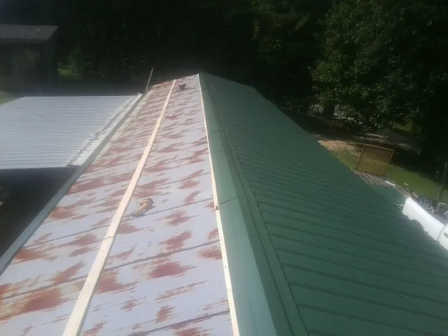 Old rusted panels beside newly installed green metal roofing — Wind Damage Roof Repair by Roofing Brothers in Santa Fe