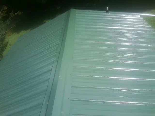 New green metal panels meeting at the ridge of a roof — Flat Roof Repair work by our crew in Santa Fe