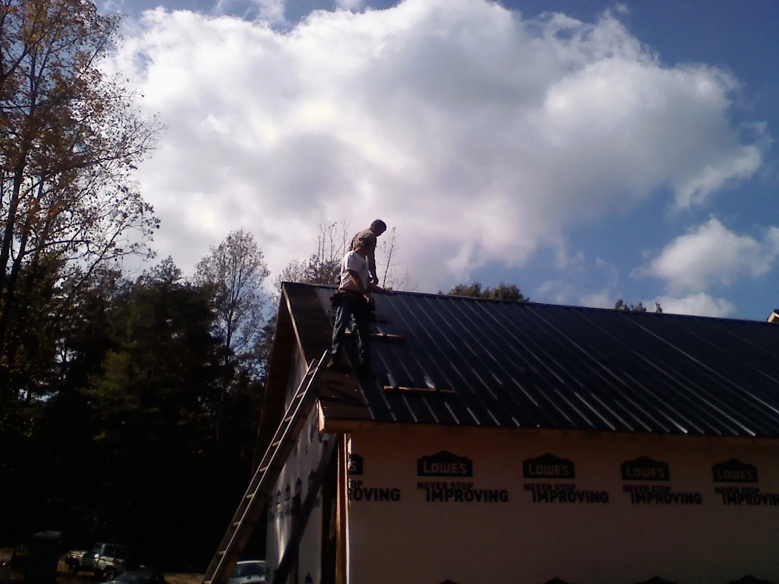 Roofer fastening dark metal panels high against a cloudy sky, from a Roof Inspection job in Santa Fe